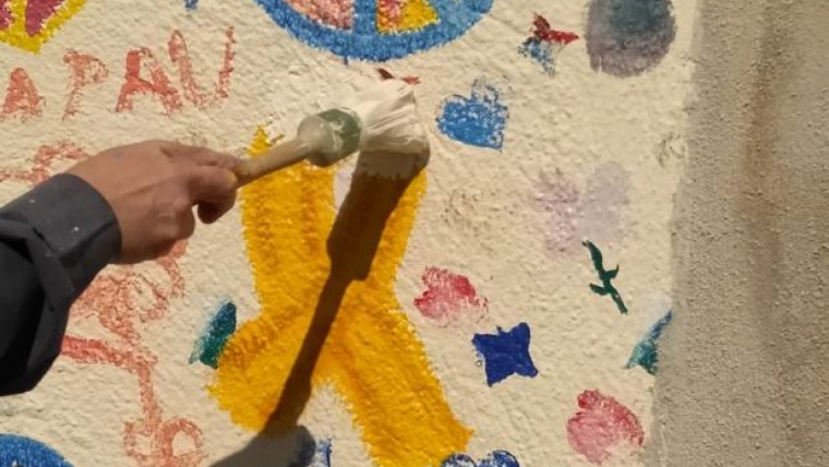 Imatge d'un agent dels Mossos traient una pintura de llaços grocs d'un mural
