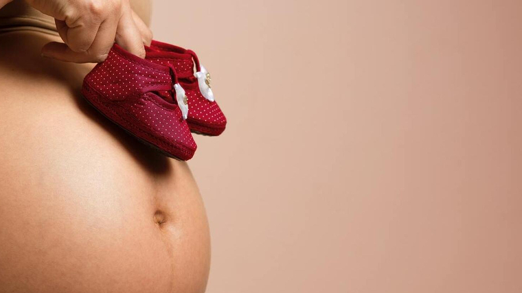 Mujer embarazada sujetando zapatos de bebÃ©