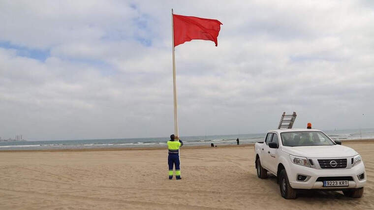 Un treballador municipal hissant la bandera roja en la platja de Cullera