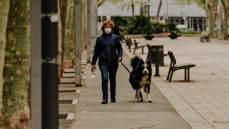 Imatge d'una dona amb mascareta passejant un gos  pels carrers de Reus