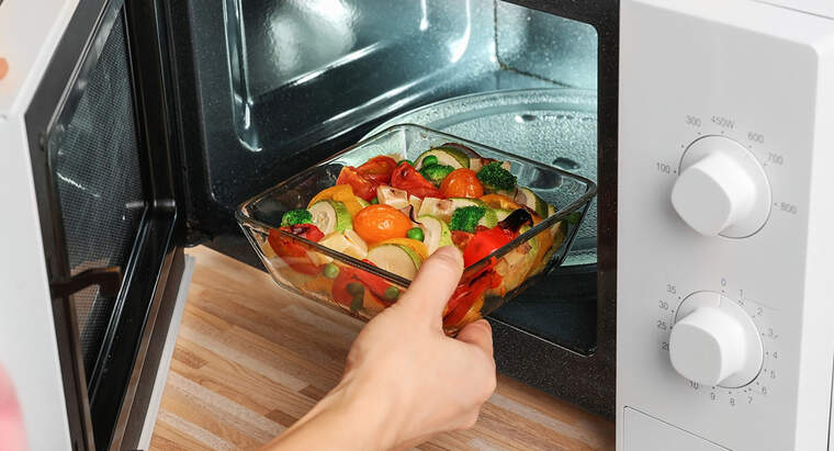 Persona introduint un plat de verdures dins d'un microones