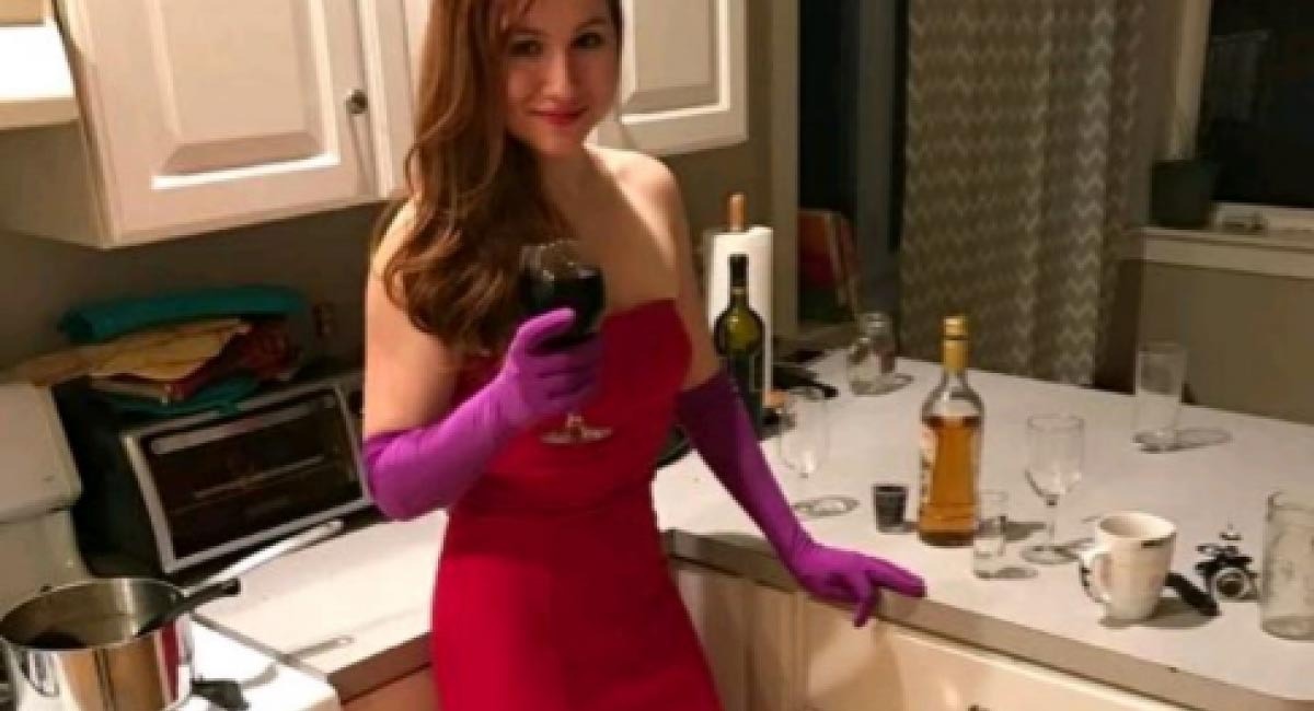 Mujer con un vestido rojo sujetando una copa en su casa.