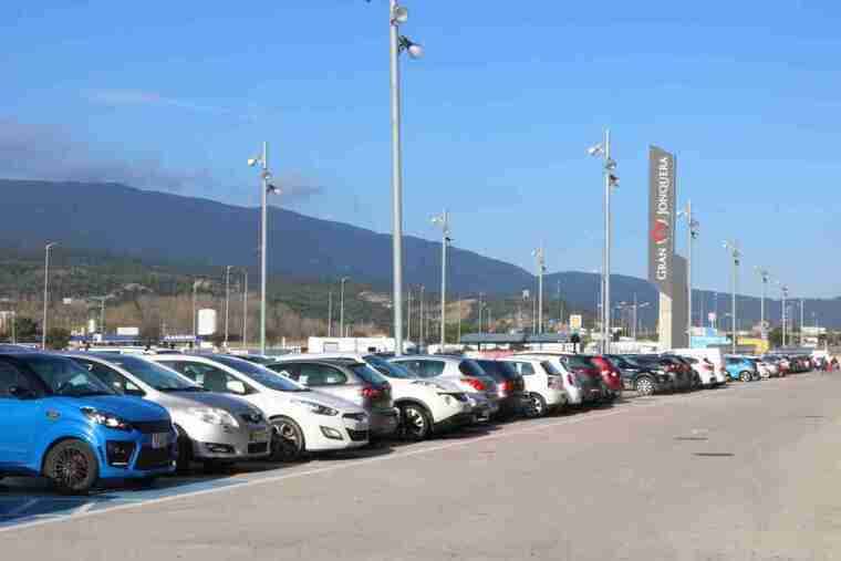 Desenes de cotxes aparcats als exteriors del Gran Outlet de la Jonquera amb els Pirineus darrere
