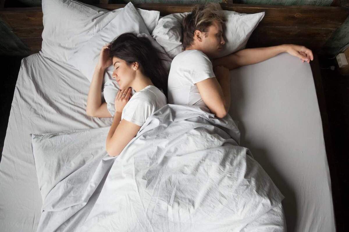 Imatge d'una parella dormint junts esquena amb esquena al mateix llit