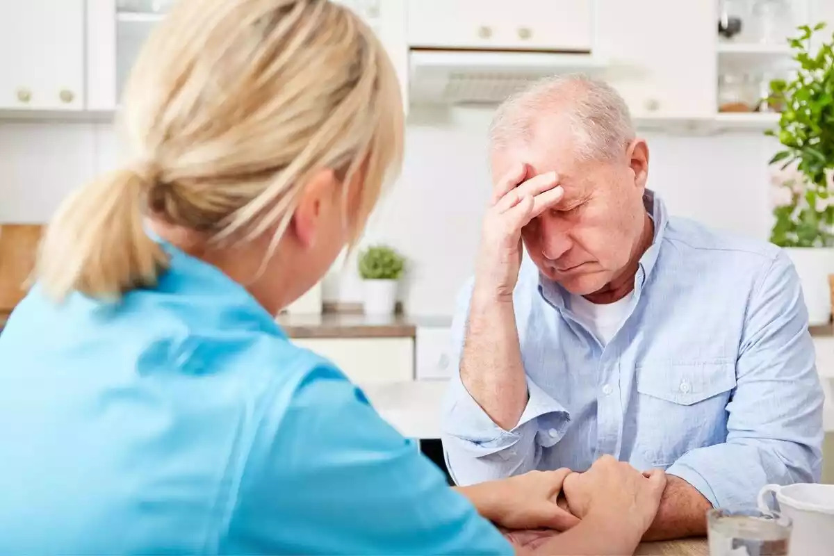 Foto d'un home gran amb mal de cap i una metgessa atenent-lo.