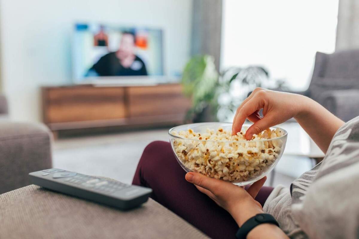 Foto d'una persona menjant crispetes mentre veu la tele.