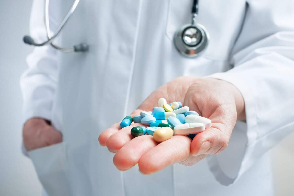 Foto d'un metge amb un munt de pastilles blaves, verdes i blanques a la mà.