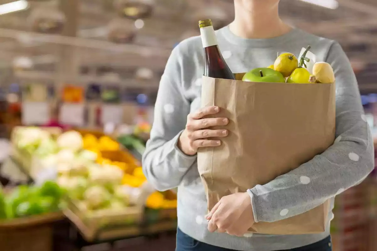 Foto d'una persona amb una bossa amb menjar en un supermercat.