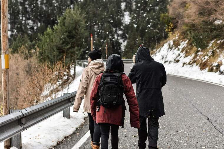 Imatge de tres persones caminant d'esquenes per una carretera nevada