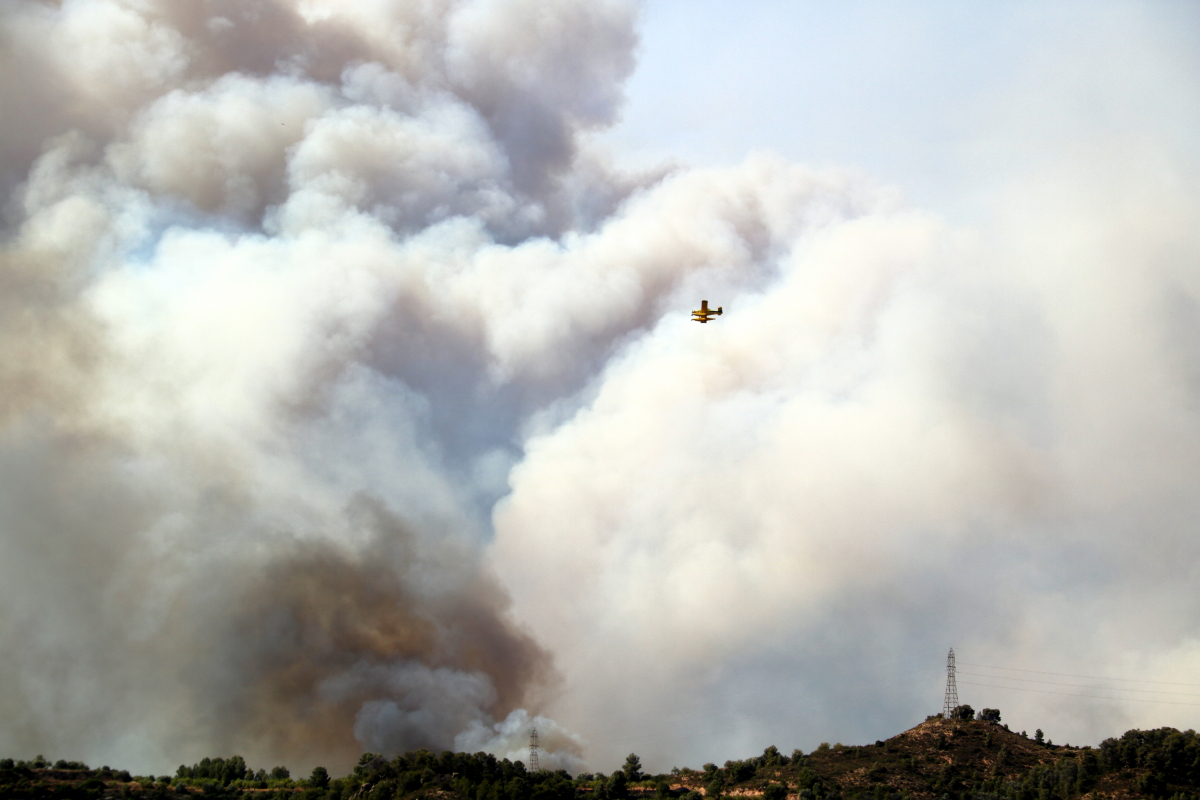 Un hidroavió sobrevola un gran núvol de fum d'un incendi forestal a la Ribera d'Ebre