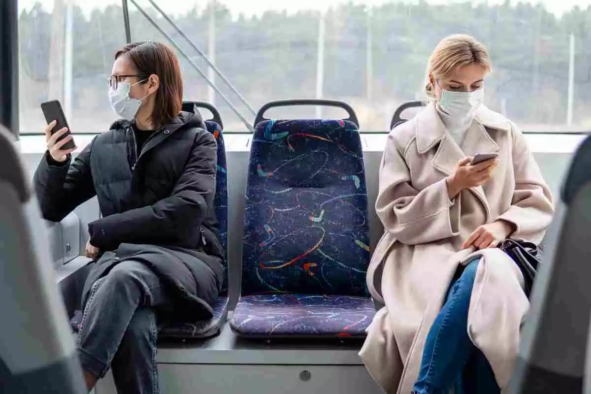 Dos mujeres con mascarilla revisan su teléfono móvil Dos mujeres con mascarilla revisan su teléfono móvil