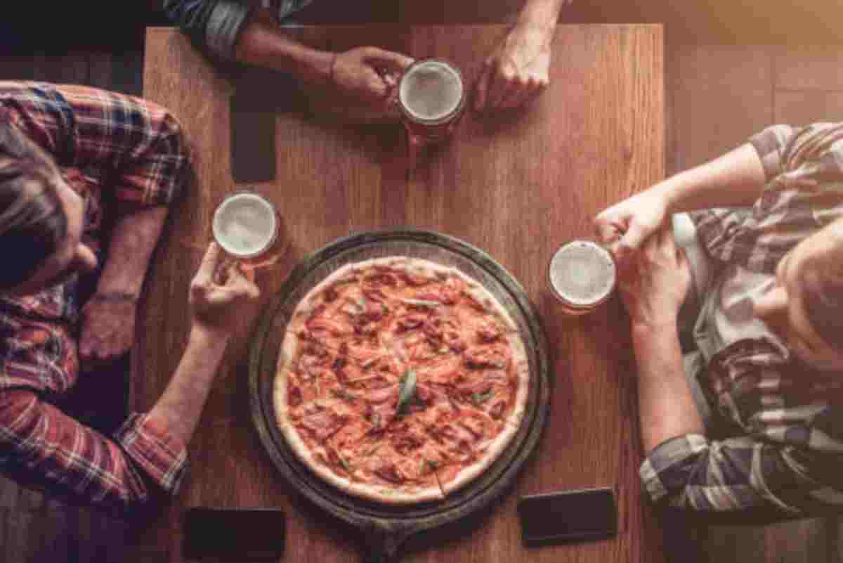 Tres jóvenes comiendo pizza en un bar y con una jarra de cerveza en la mano