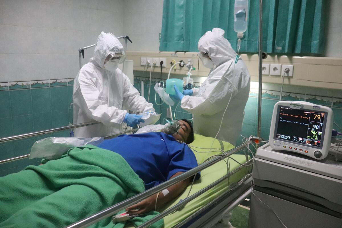Pacient de Covid intubat i atès per dos professionals de la sanitat vestits de blanc, altament protegits