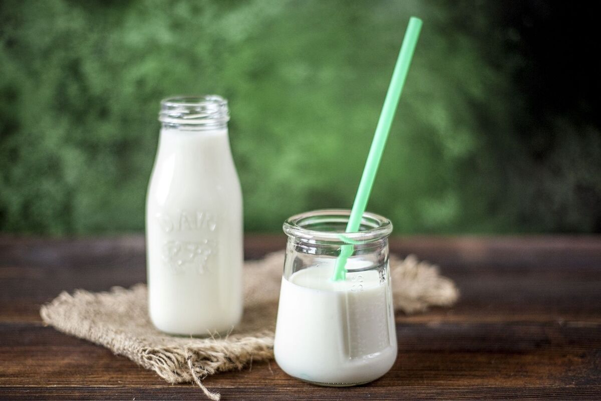 Un vaso y una botella de leche sobre una mesa de madera con fondo verde