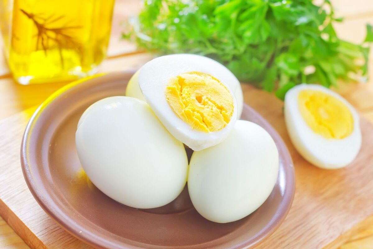 Varios huevos blancos cocidos con la yema amarilla a la vista y perejil detrás Varios huevos blancos cocidos con la yema amarilla a la vista y perejil detrás