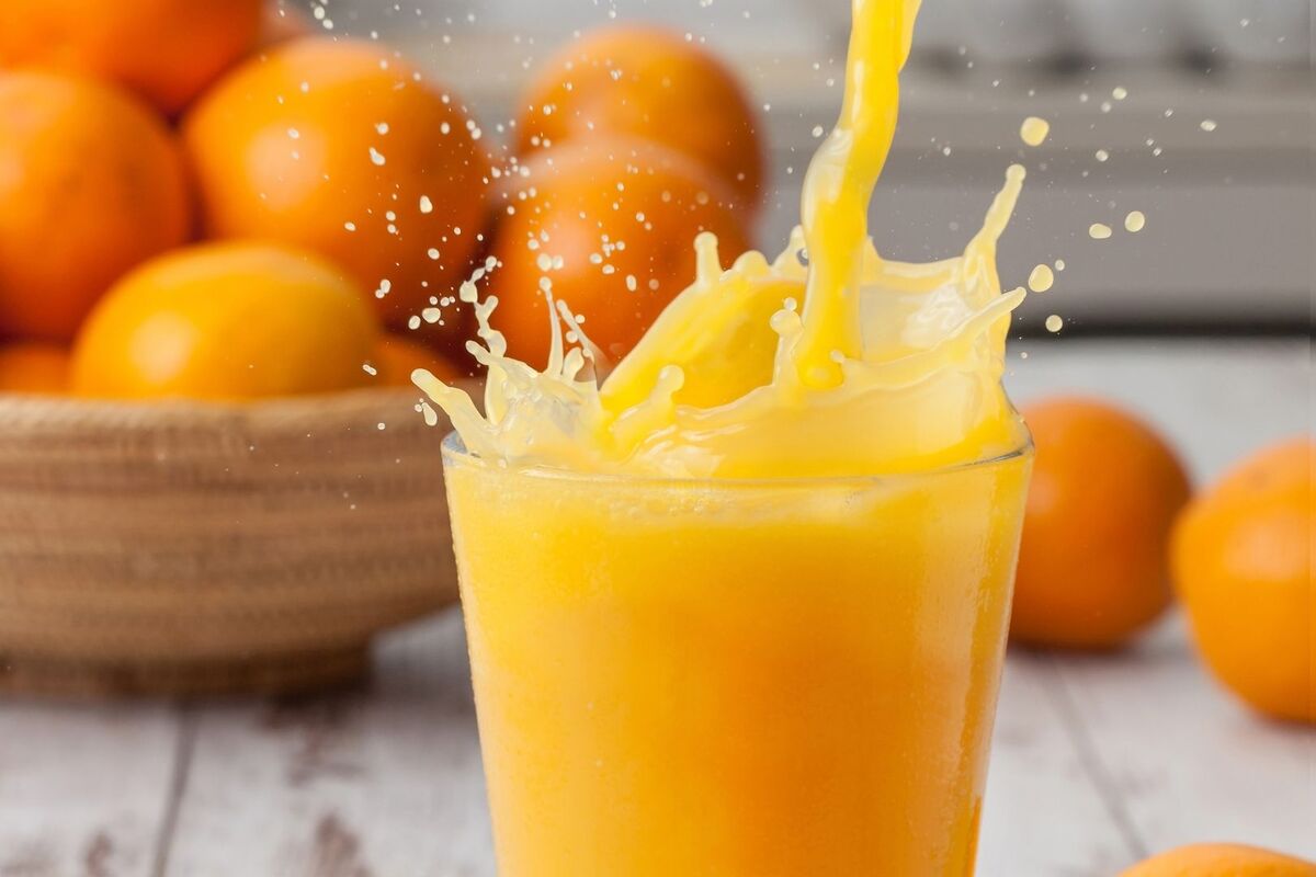 Zumo de naranja exprimido en un vaso con varias frutas detrás