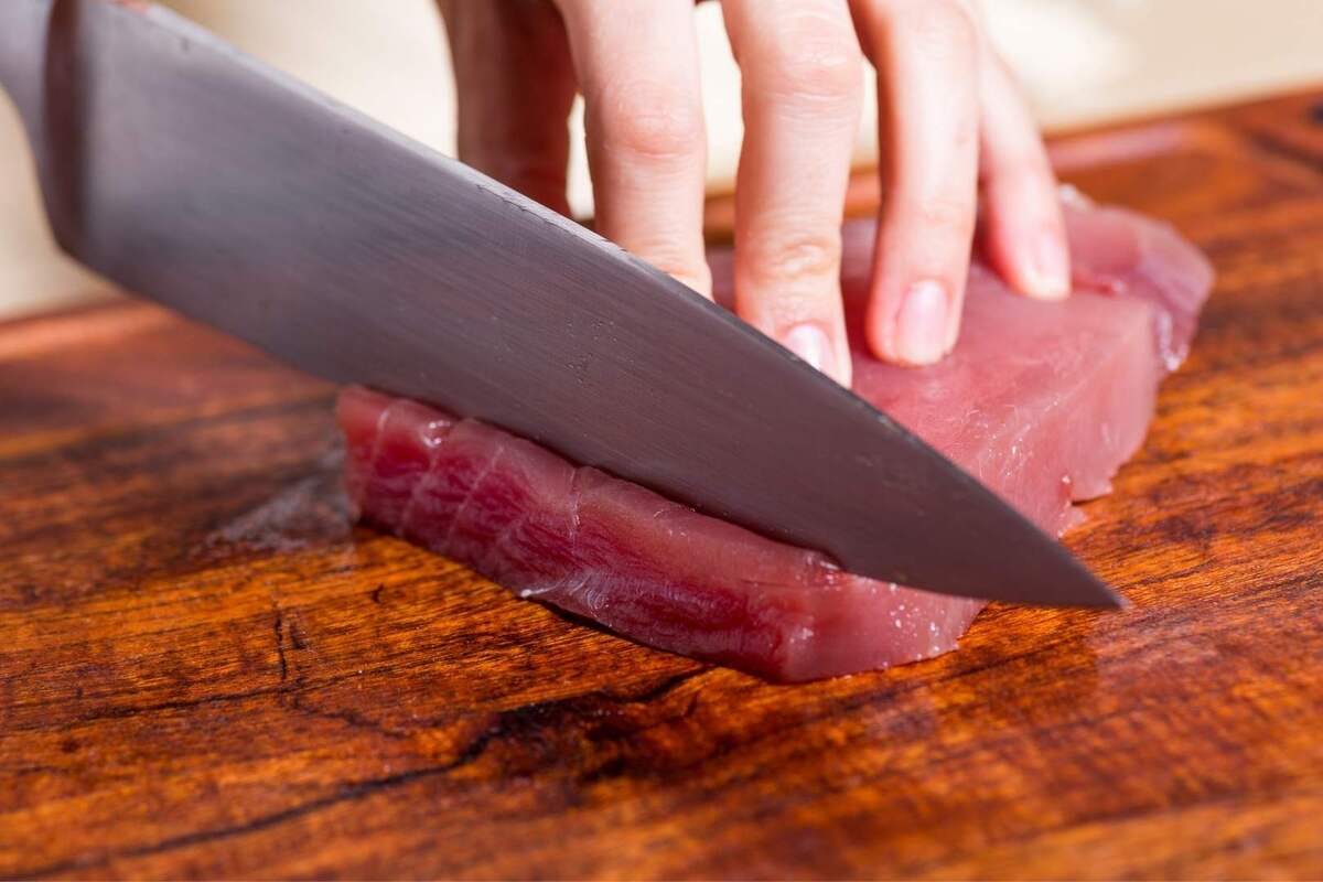 Mano cortando con un cuchillo grande atún rojo en una tabla de madera