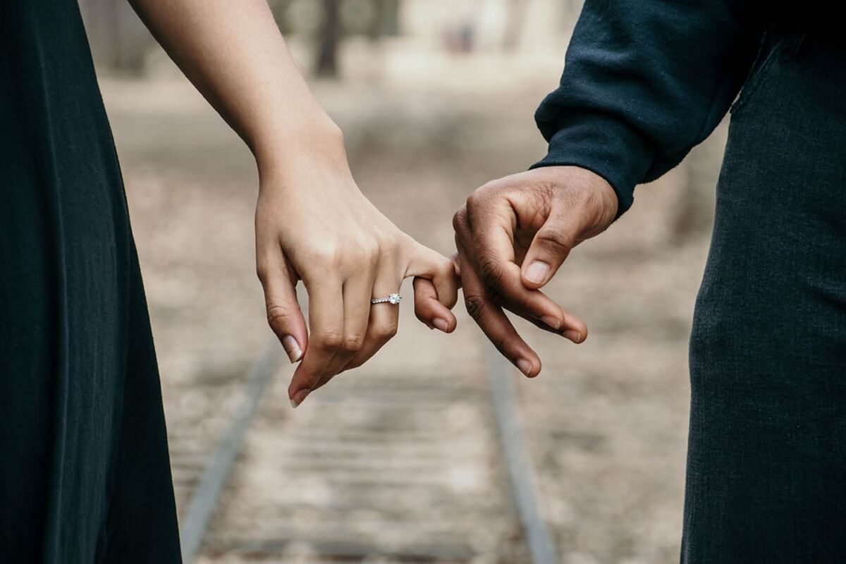Una pareja cogida con los dedos de la mano sobre unas vías de tren Una pareja cogida con los dedos de la mano sobre unas vías de tren