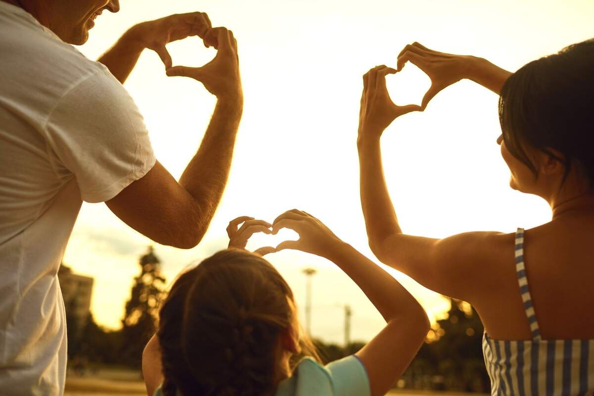 Tres personas de espaldas formando un corazón con sus manos en un atardecer Tres personas de espaldas formando un corazón con sus manos en un atardecer