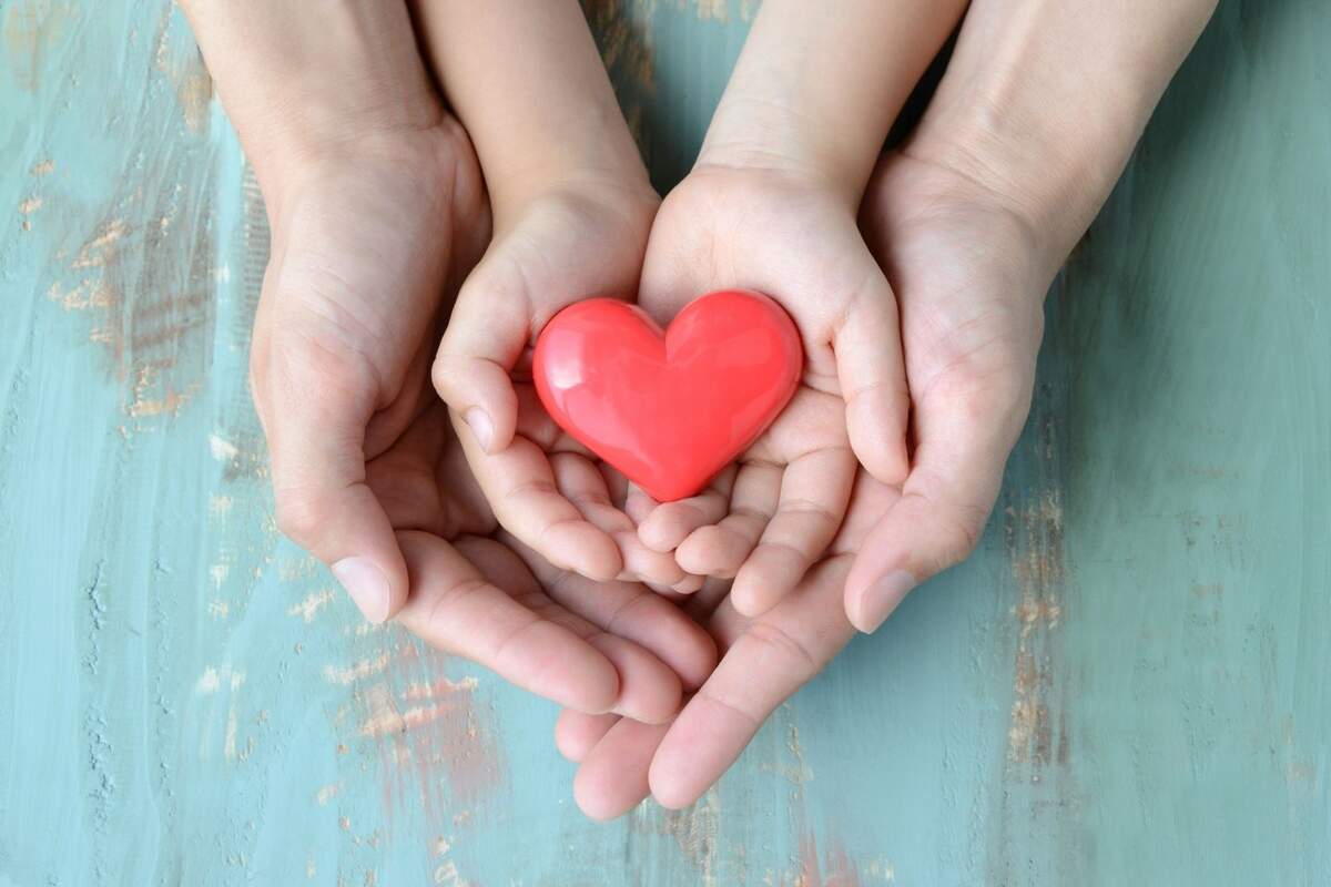 Una mano de adulto y otra de un niño, sosteniendo una figura en forma de corazón Una mano de adulto y otra de un niño, sosteniendo una figura en forma de corazón