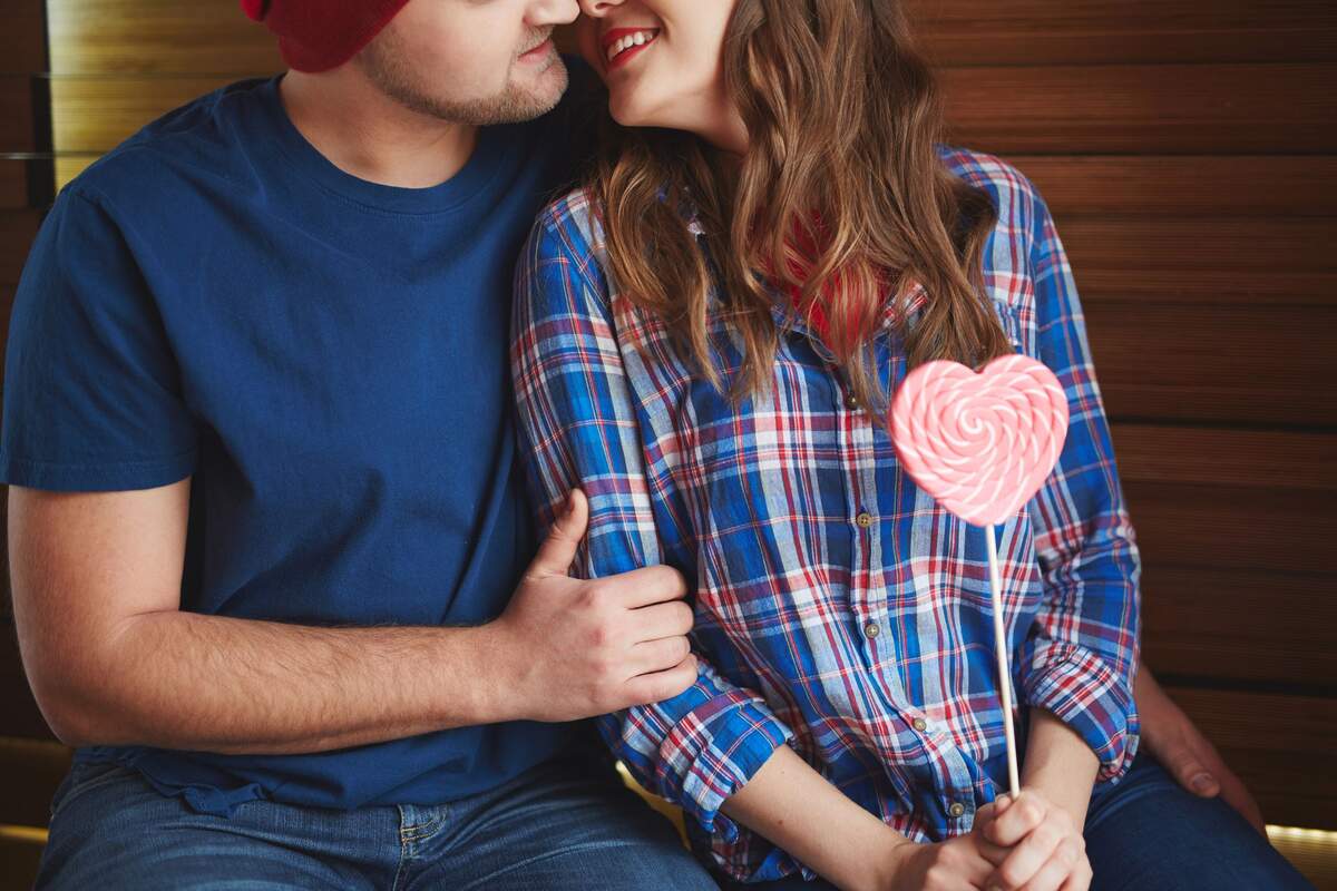 Una pareja a punto de besarse con una piruleta en la mano en forma de corazón