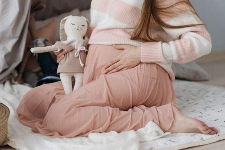 Chica vestida de rosa sujeta su vientre y un conejo