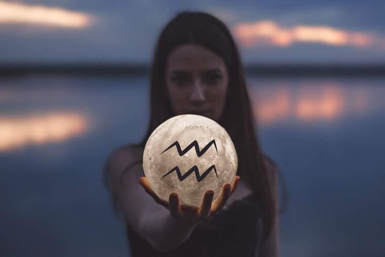 Imagen de una mujer sosteniendo una Luna con la mano derecha que tiene el símbolo de Acuario