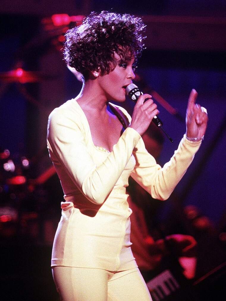 La cantante Whitney en un concierto vestida de blanco y con gente detrás
