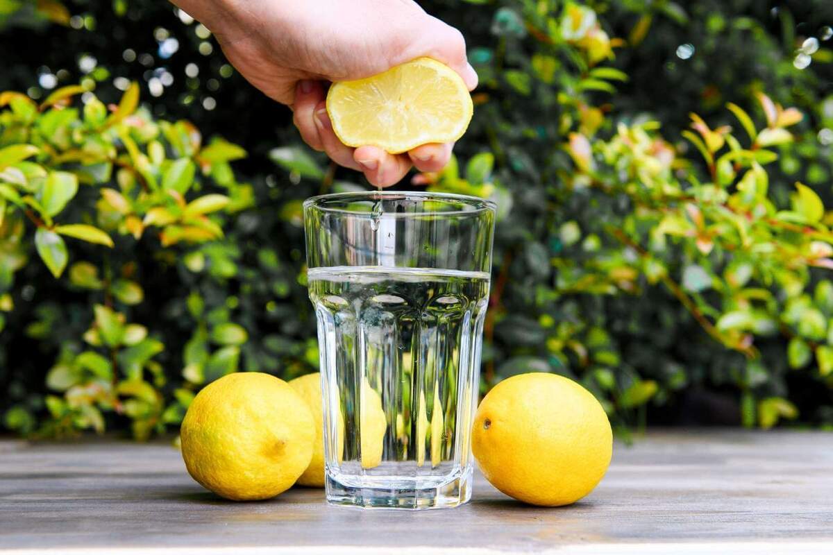 Mano exprimiendo medio limón en un vaso transparente con agua