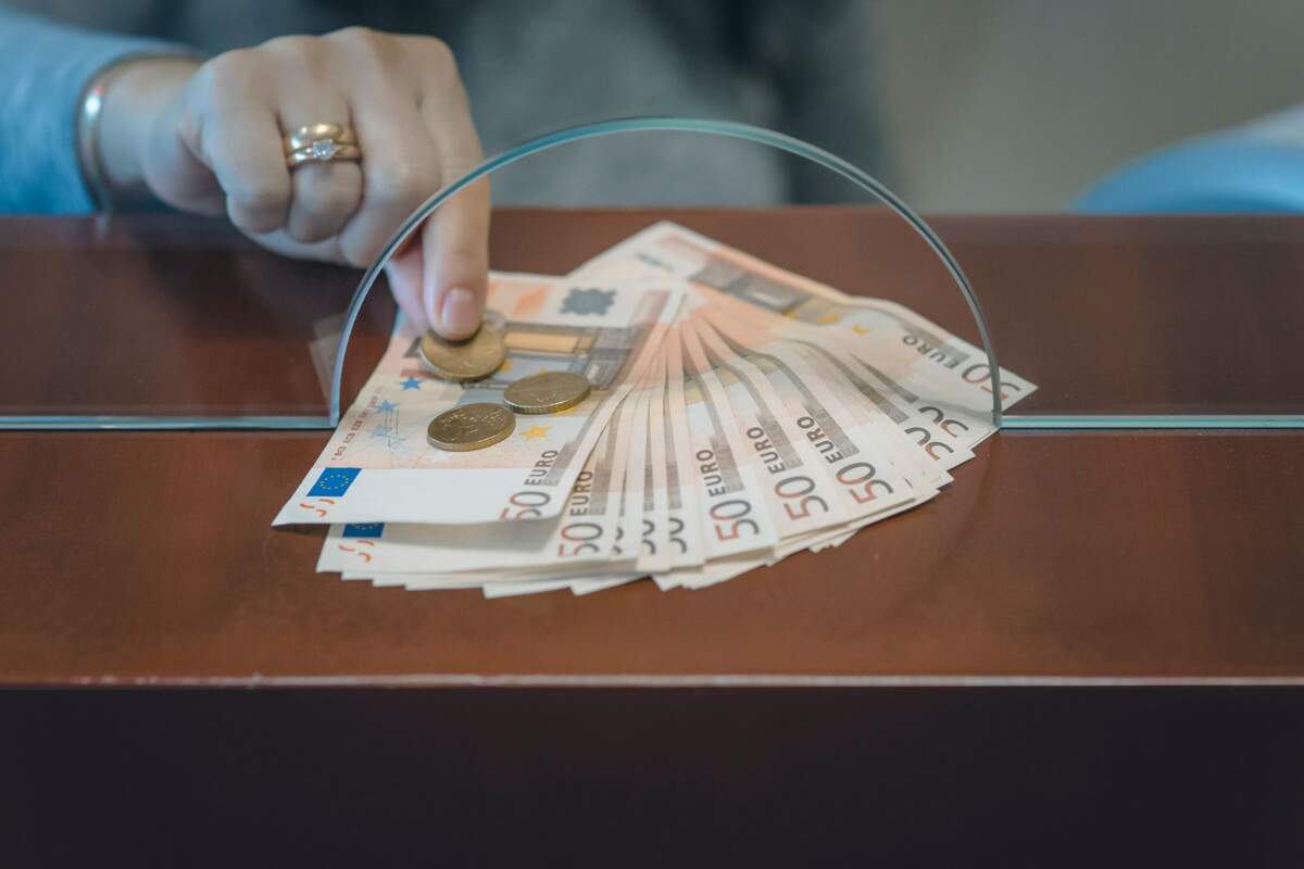 Una mujer recoge dinero y mondas de euro a través de una ventanilla