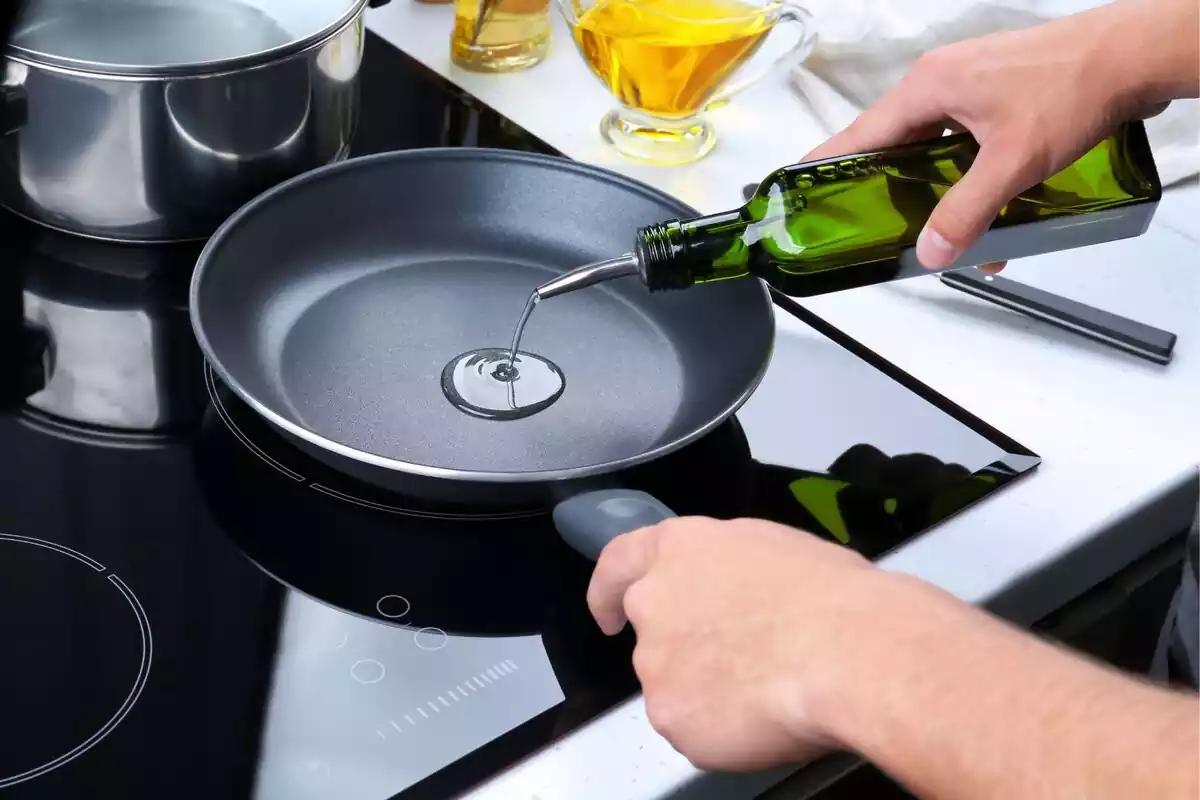 Una persona añadiendo aceite en una sartén de cocina colocada en una vitro Una persona añadiendo aceite en una sartén de cocina colocada en una vitro