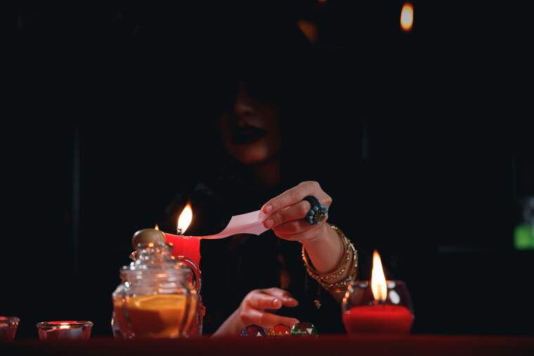 Woman burning a piece of paper with the fire of a candle