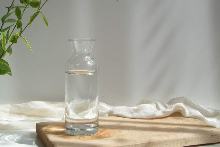 Jarra de cristal con agua, encima de una madera sobre fondo blanco