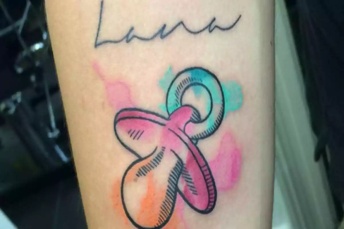 Detalle frontal de tatuaje de nombre Lana con un chupete en colores de acuarela Detalle frontal de tatuaje de nombre Lana con un chupete en colores de acuarela
