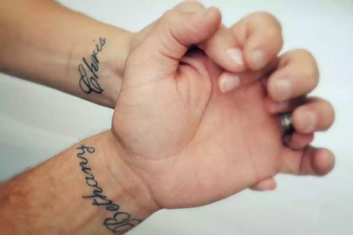 Diseño de tatuajes en la muñeca con dos nombres y unas manos entrelazadas Diseño de tatuajes en la muñeca con dos nombres y unas manos entrelazadas