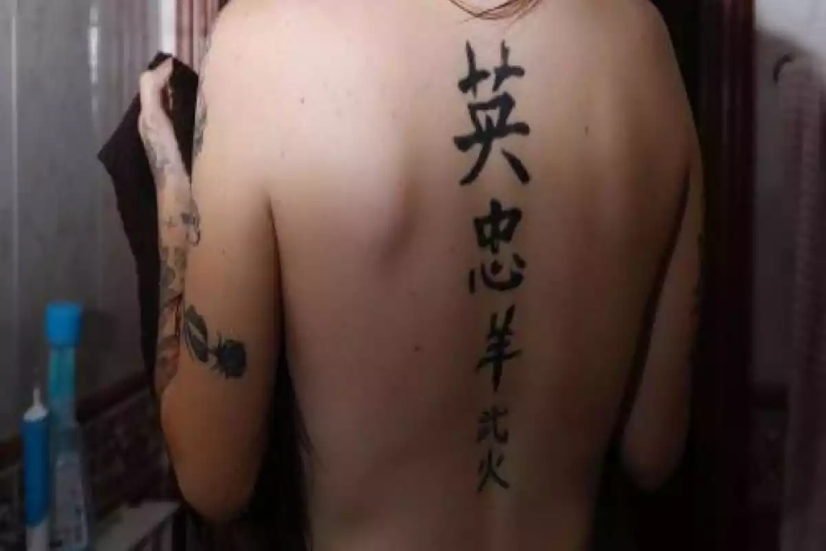Diseño espalda tatuada con letras chinas en semi oscuridad Diseño espalda tatuada con letras chinas en semi oscuridad