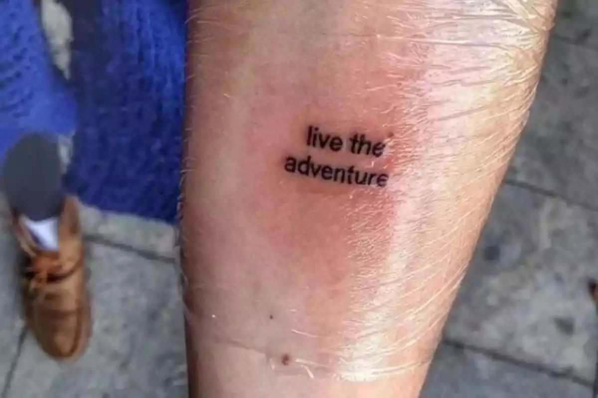 Foto con detalle de un brazo en el que aparece un tatuaje recién hecho envuelto en plástico con la frase en inglés 'Live the adventure' Foto con detalle de un brazo en el que aparece un tatuaje recién hecho envuelto en plástico con la frase en inglés 'Live the adventure'