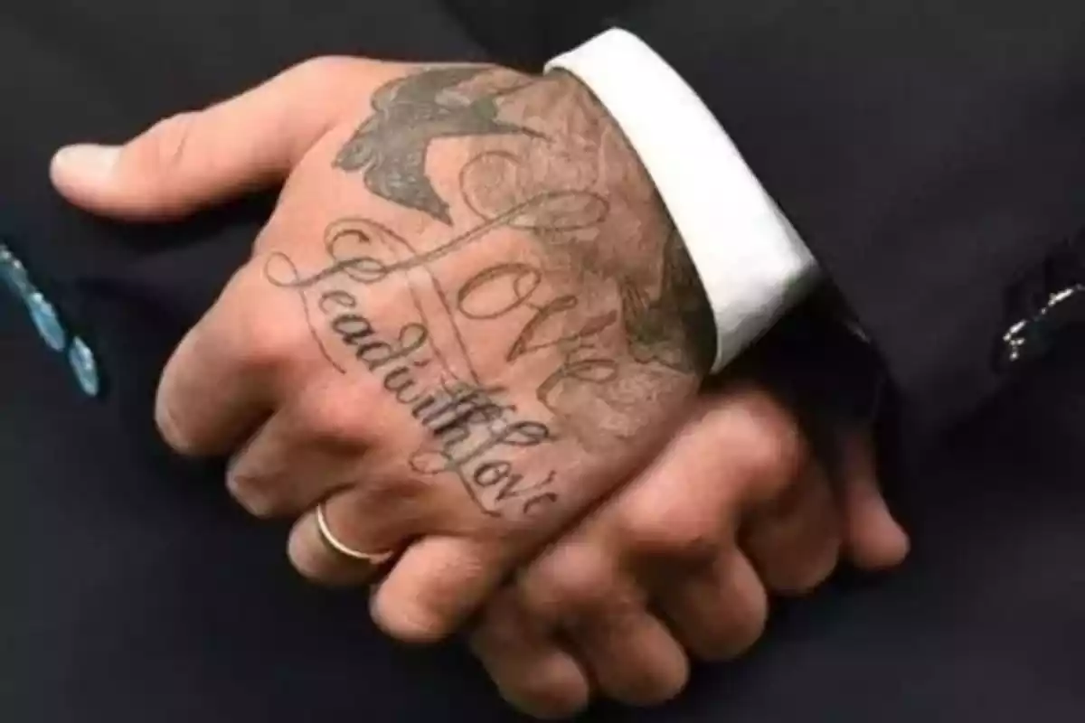 Foto con detalle de unas manos entrelazadas y una de ellas lleva un tatuaje en el que aparece la frase en tinta negra 'El amor lidera con amor' Foto con detalle de unas manos entrelazadas y una de ellas lleva un tatuaje en el que aparece la frase en tinta negra 'El amor lidera con amor'