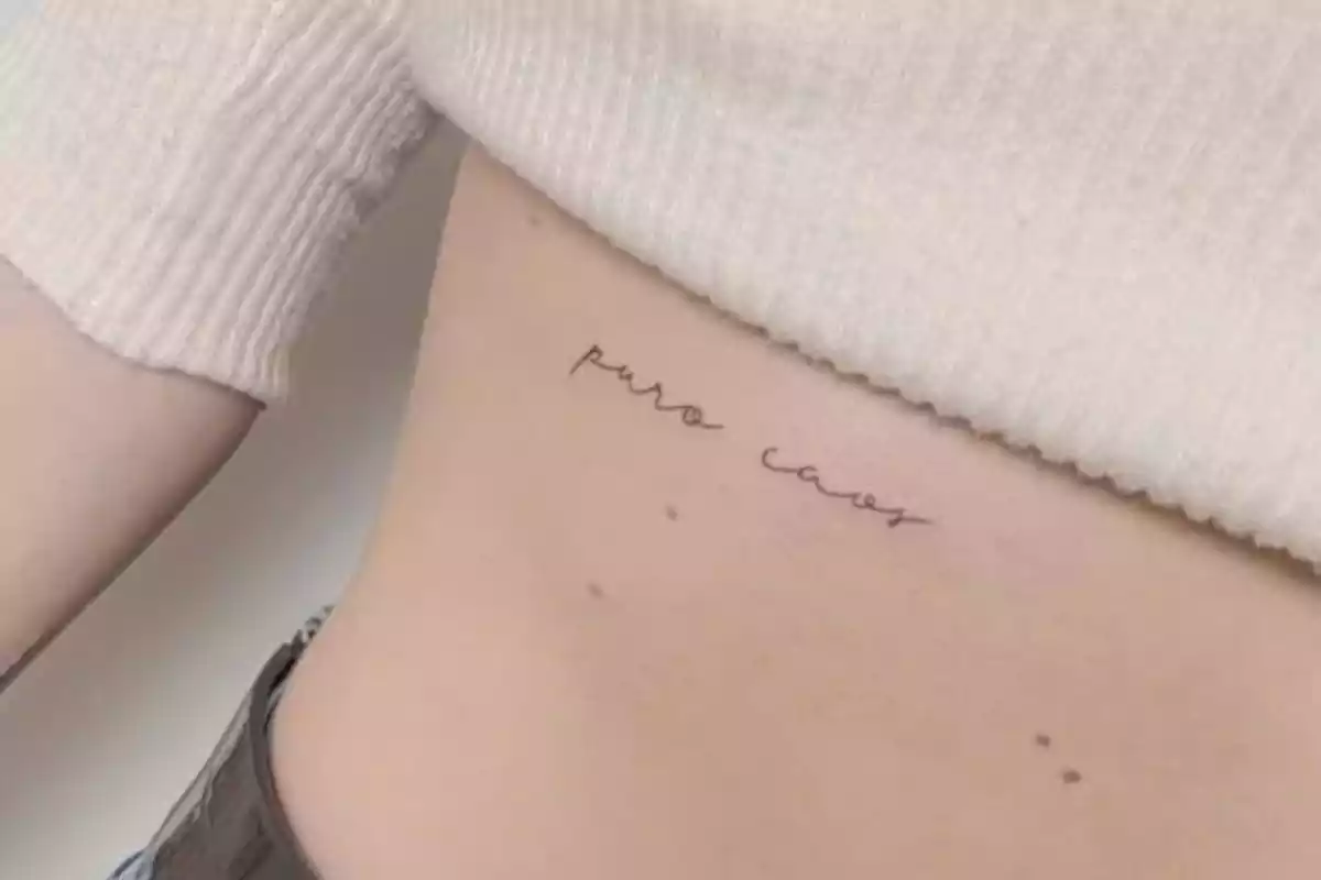 Foto de un abdomen femenino recortada en la que aparece un tatuaje en tinta negra con la frase 'Puro Caos' Foto de un abdomen femenino recortada en la que aparece un tatuaje en tinta negra con la frase 'Puro Caos'
