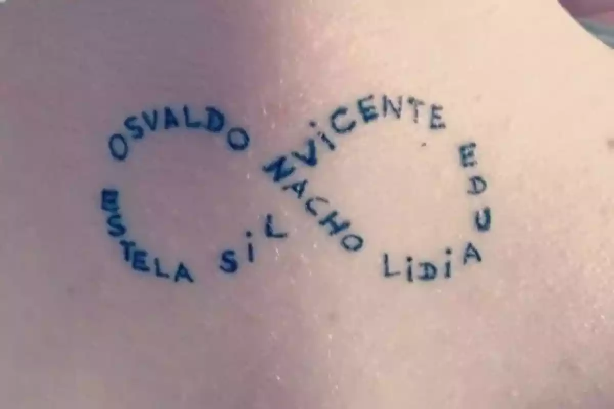 Foto de un tatuaje con símbolo de infinito formado por varios nombres en color negro Foto de un tatuaje con símbolo de infinito formado por varios nombres en color negro