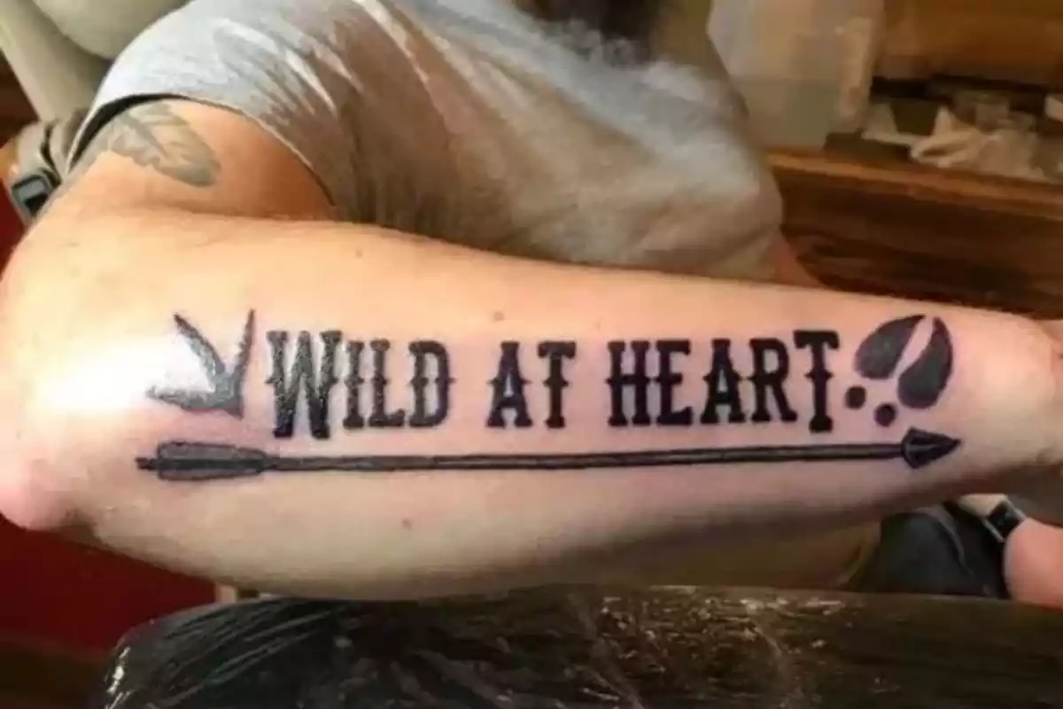 Foto del brazo de un hombre que lleva un tatuaje con la frase en inglés 'Wild at heart' Foto del brazo de un hombre que lleva un tatuaje con la frase en inglés 'Wild at heart'