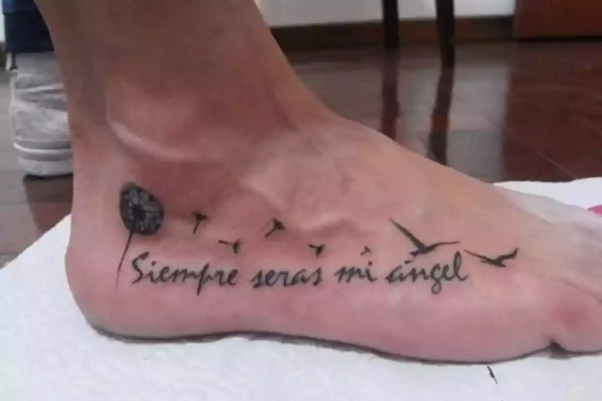 Foto detalle de un pie en el que aparece un tatuaje en tinta negra con la frase 'Siempre serás mi ángel' Foto detalle de un pie en el que aparece un tatuaje en tinta negra con la frase 'Siempre serás mi ángel'