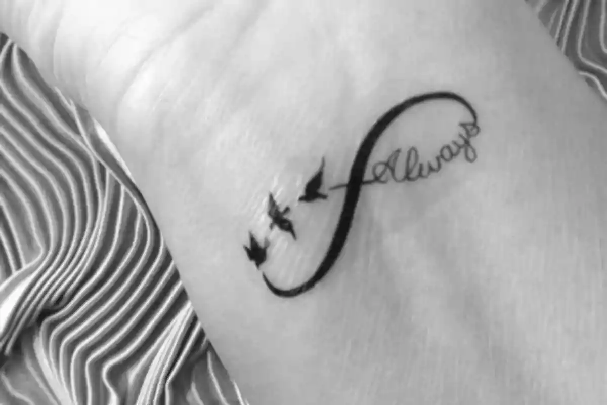 Foto en blanco y negro de un brazo con detalle de la muñeca en el que aparece el símbolo de infinito con la palabra 'Always' y unos pájaros Foto en blanco y negro de un brazo con detalle de la muñeca en el que aparece el símbolo de infinito con la palabra 'Always' y unos pájaros