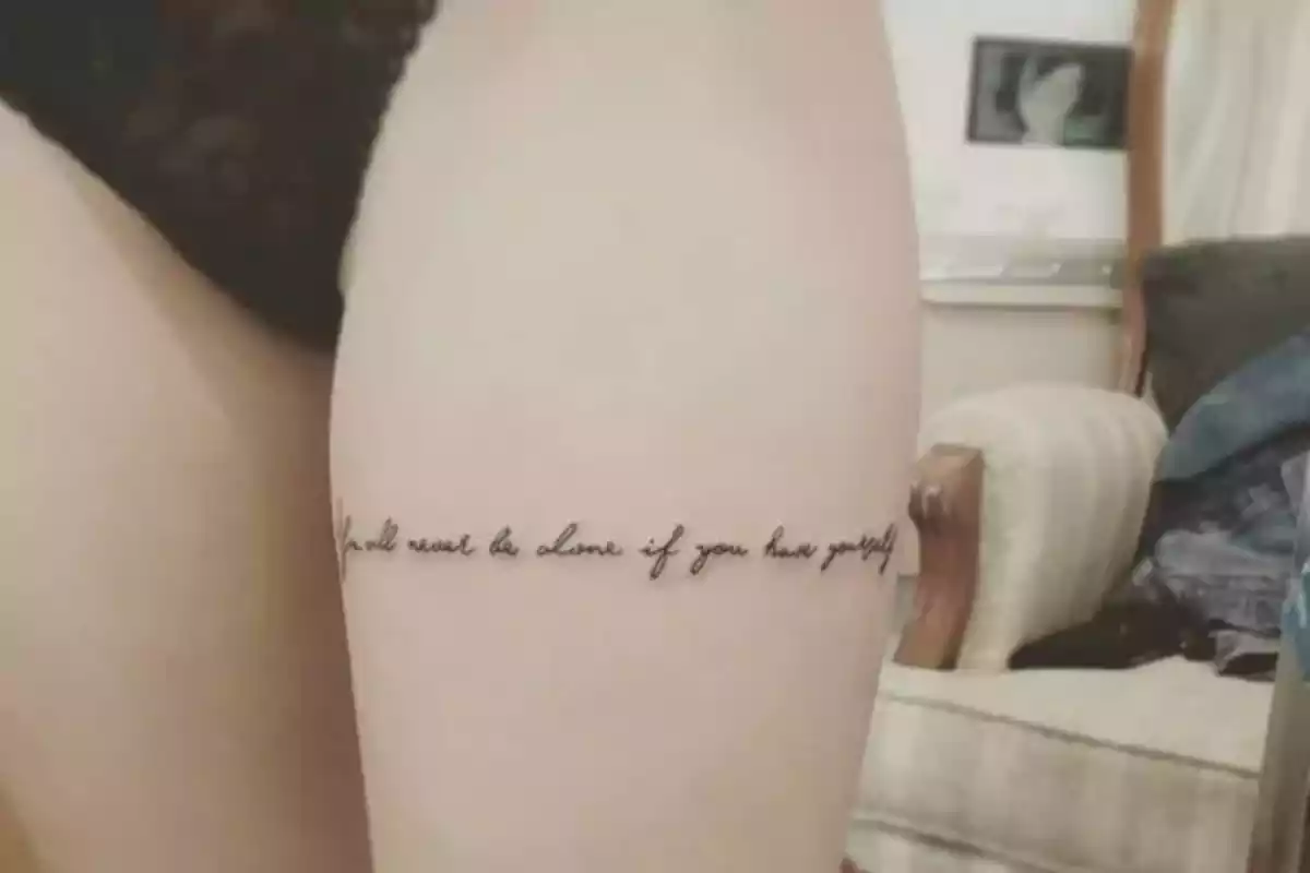 Foto recortada de una mujer con detalle de sus muslos y uno de ellos con la frase en inglés 'Nunca estarás solo si te amas a ti mismo' Foto recortada de una mujer con detalle de sus muslos y uno de ellos con la frase en inglés 'Nunca estarás solo si te amas a ti mismo'
