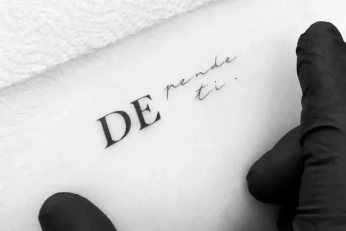Foto recortada en blanco y negro en la que un guante en negro sujeta un brazo con el tatuaje de la frase 'Depende de ti' Foto recortada en blanco y negro en la que un guante en negro sujeta un brazo con el tatuaje de la frase 'Depende de ti'