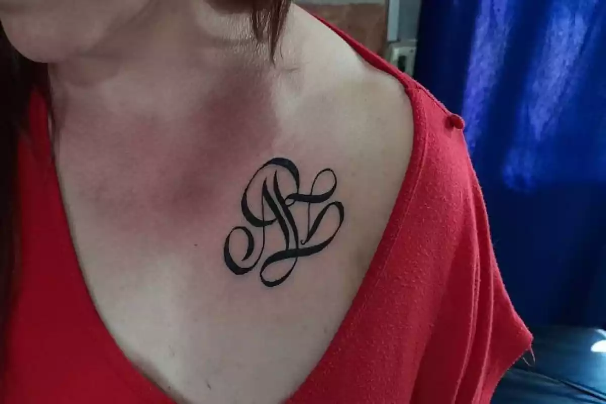 Tatuaje de unas letras o iniciales en la clavícula de una mujer con una camiseta roja Tatuaje de unas letras o iniciales en la clavícula de una mujer con una camiseta roja