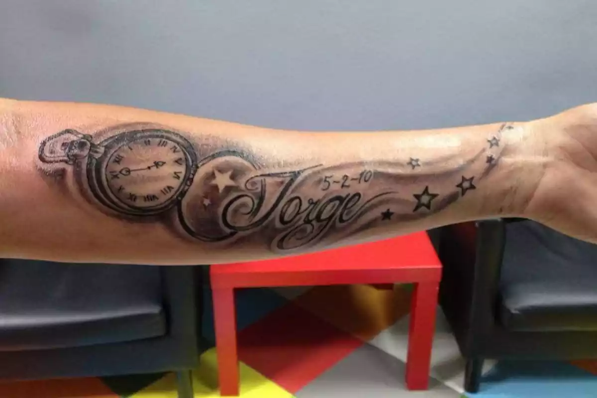 Tatuaje nombre en un brazo con un dibujo de estrellas y un reloj Tatuaje nombre en un brazo con un dibujo de estrellas y un reloj