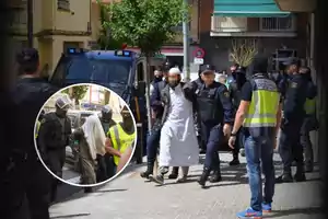 Varios agentes de policía escoltan a un hombre esposado vestido con ropa blanca en una calle urbana mientras otras personas observan y en un recuadro se muestra a otro detenido custodiado por la Guardia Civil