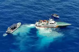 Barco de la Guardia Civil y otra embarcación pequeña en el mar junto a una patera con varias personas