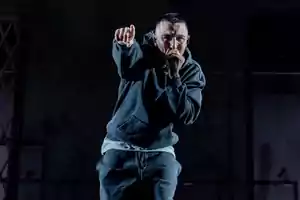 Rapero con sudadera gris cantando y señalando al público durante un concierto